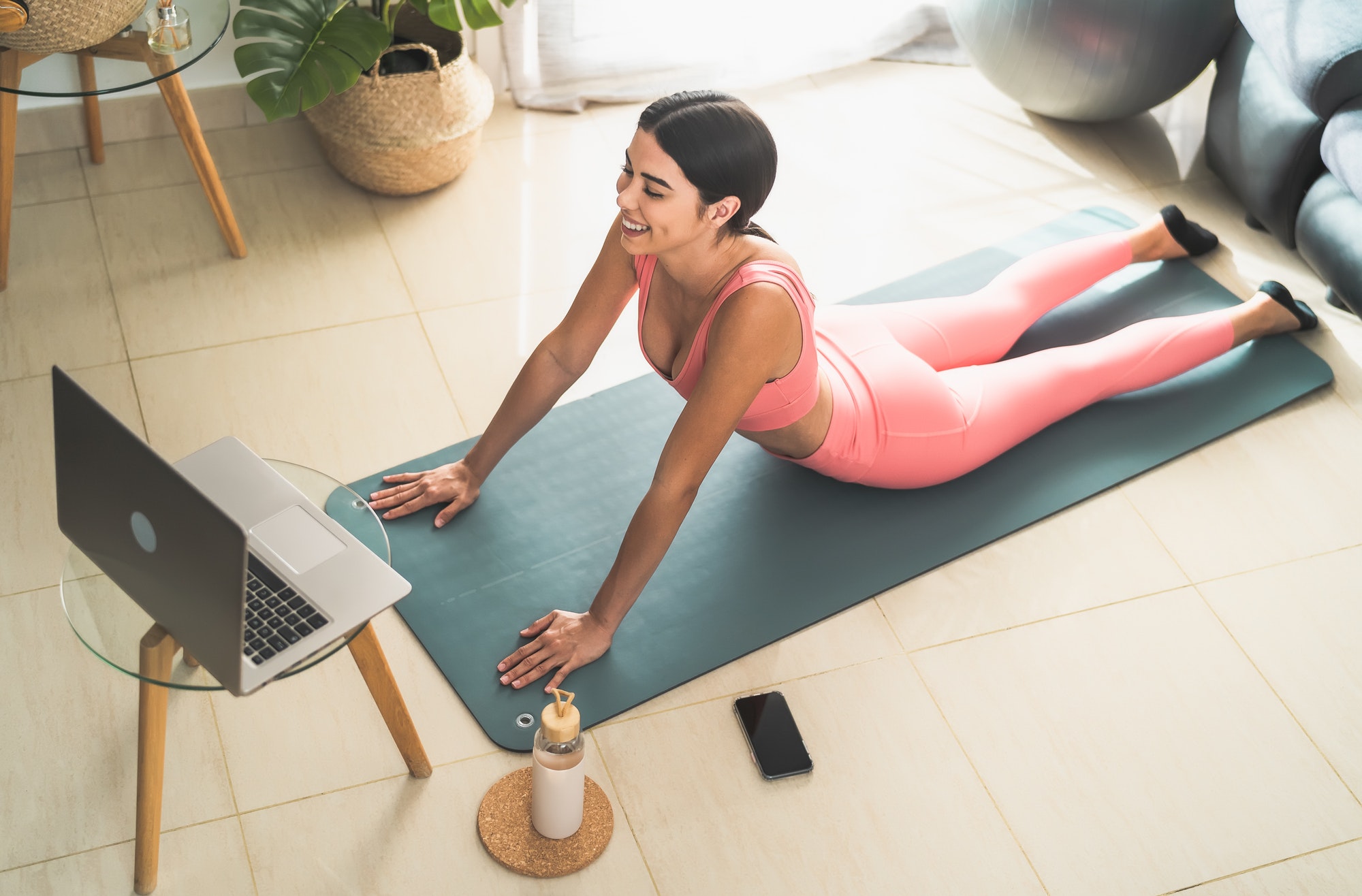 Young Latin woman doing pilates virtual fitness class with laptop at home
