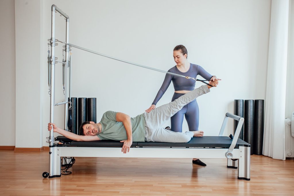 Reformer Pilates An attractive man working out with a pilates instructor in the gym
