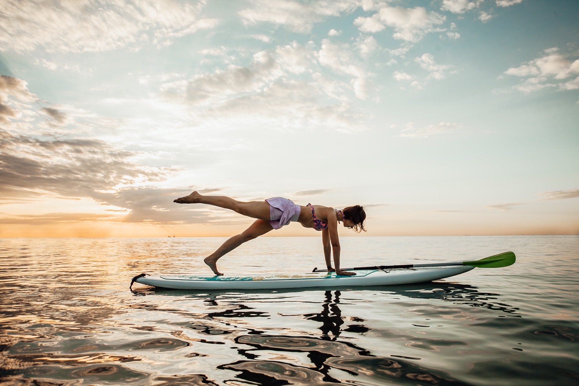 Young woman doing Pilates on a SUP board in the lake at sunrise