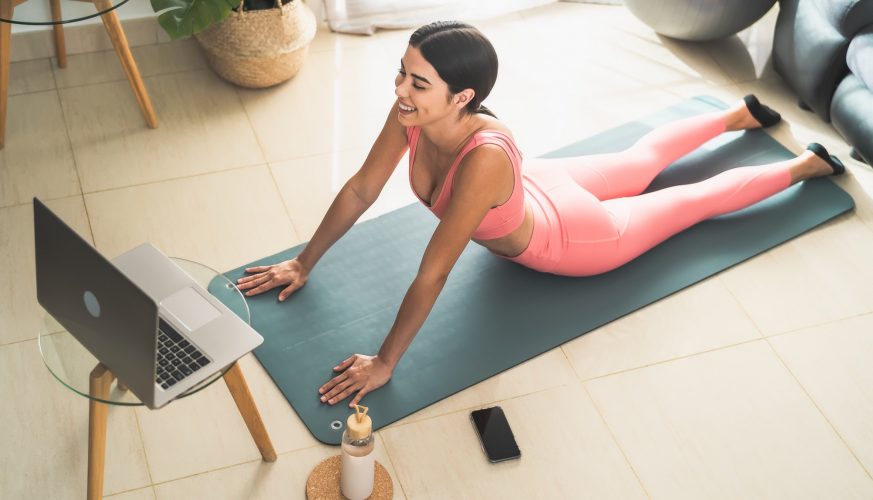 Young Latin woman doing pilates virtual fitness class with laptop at home
